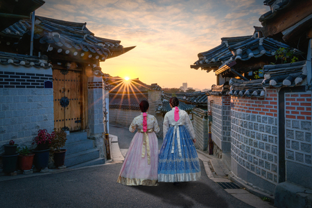 Back of two women wearing hanbok walking through the traditional style houses of Bukchon Hanok Village in Seoul, South Korea.のeditorial素材
