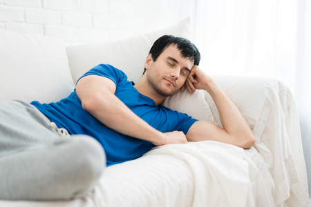 Time to relax. Handsome young man sleeping on the white sofa  at home.

の写真素材