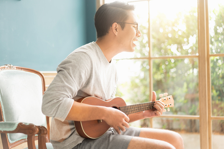 Asian young man hands playing acoustic guitar ukulele at home. Enjoy playing acoustic guitar sunshine in the evening.

の写真素材