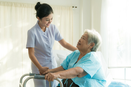 Asian young nurse supporting elderly patient disabled woman in using walker in hospital. Elderly patient care concept.