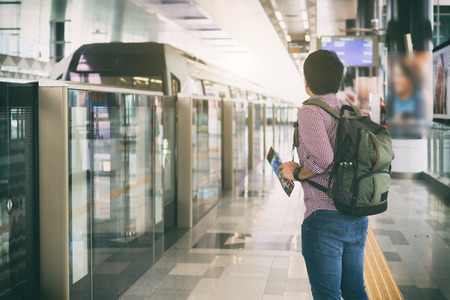 Young man traveler with backpack holding Kuala Lumpur location map in hands while looking MRT Train coming to platform in Kuala Lumpur, Malaysia.の写真素材