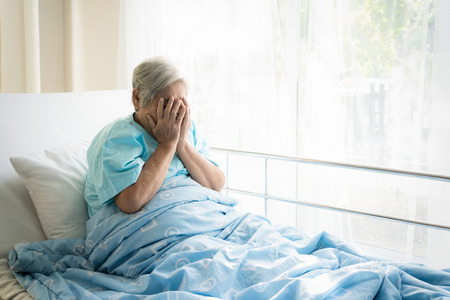 Asian depressed elderly woman patients lying on bed looking out the window in hospital. Elderly woman patients is glad recovered from the illness.の写真素材