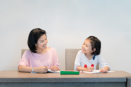 Happy Asian family. Asian Mother and daughter together drawing and paint in book. Adult woman helps...