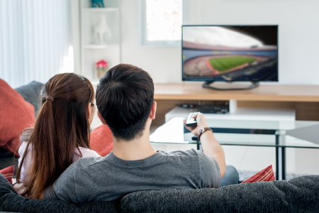 Rear view of Asian couple watching football at television in living room. Football festival concept.の写真素材