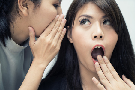 Two Asian woman gossip revealing secret to her friend in office. People communication and friendship conceptの写真素材