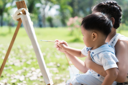 Asian little boy and sister draw together in park. Kids painting and drawing. Children paint with paintbrush color and pencils. Art and crafts for toddler and preschooler.の写真素材