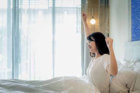 Asian Woman stretching in bed after wake up in bedroom at home.の写真素材