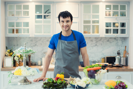 Handsome man cooking at home preparing salad in kitchen. Healthy eating, vegetarian food, diet and people conceptの写真素材