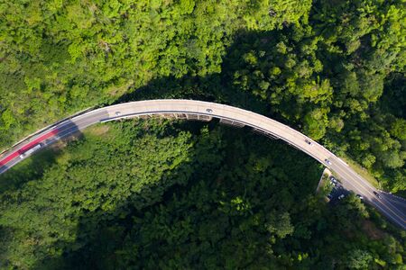 Aerial view over mountain road going through tropical rainforest landscape in Thailand.