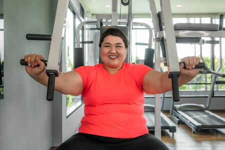 Asian Overweight woman playing Gym Equipment to exercising build her boday alone in gym, happy and smile during workout. Fat women take care of health and want to lose weight concept.の写真素材