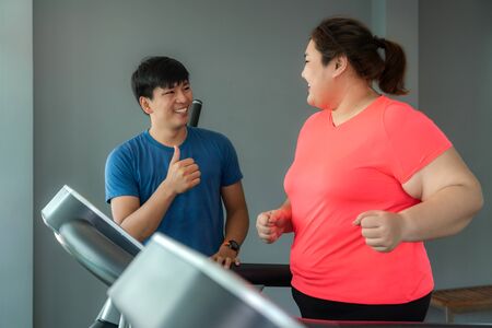 Two Asian trainer man and Overweight woman exercising training on treadmill in gym, trainer thump up to her for good result during workout. Fat women take care of health and want to lose weight concept.の写真素材