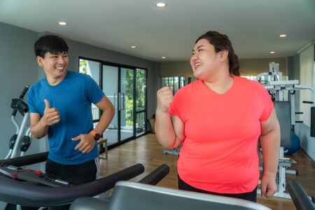 Two Asian trainer man and Overweight woman exercising training on treadmill in gym, trainer thump up...