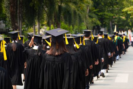 Rear view of group of university graduates in black gowns lines up for degree in university graduation ceremony. Concept education congratulation, student, successful to study.の写真素材