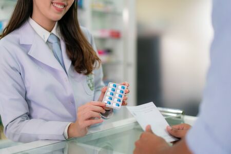 Confident Asian young female pharmacist with a lovely friendly smile and explaining capsule medicine to her customer in the pharmacy drugstore. Medicine, pharmaceutics, health care and people concept.の写真素材