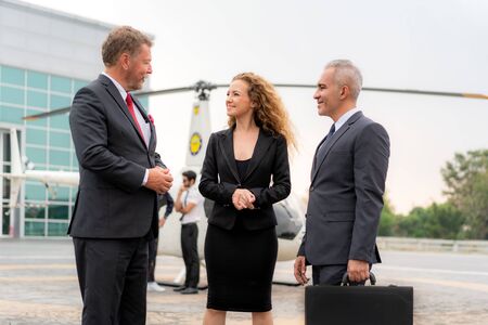 Three Businesswoman And Businessman In Discussion with Briefcase standing near helicopter when he arrive destination at helipad in airport with helicopter and captain standing near in background. の写真素材