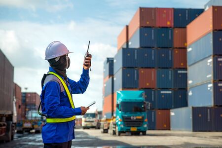 Foreman using and talking walkie talkie to control loading Containers box to truck at Container...