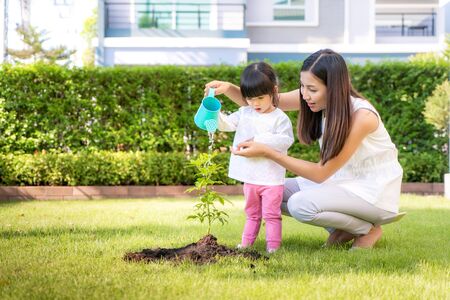 Asian family mother and kid daughter plant sapling tree and watering outdoors in nature spring for reduce global warming growth feature and take care nature earth. People kid girl in garden background.の写真素材