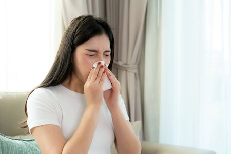 Asian woman sick and sad with sneezing on nose and cold cough on tissue paper because influenza and weak or virus bacteria from dust weather or smoke for medical.の写真素材