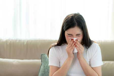 Asian woman sick and sad with sneezing on nose and cold cough on tissue paper because influenza and weak or virus bacteria from dust weather or smoke for medical.
の写真素材
