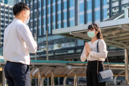 Pay respect is new novel greeting to avoid the spread of coronavirus. Two Asian young businessman and businesswoman friends meet in font of office building. Instead of greeting with a hug or handshake, they Pay respect instead.の写真素材
