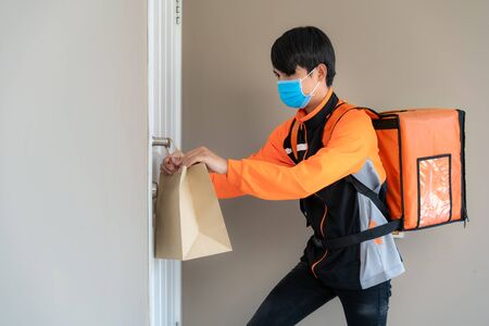 Asian delivery man send food bag at door knob for contactless or contact free from delivery rider in front house for social distancing for infection risk.の写真素材