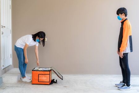 Asian woman unpacking and pick up delivery food bag from box and for contactless or contact free from delivery rider with bicycle in front house for social distancing for infection risk.の写真素材