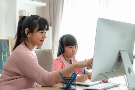Asian girl student with mother video conference e-learning with teacher on computer in living room at home. Homeschooling and distance learning ,online ,education and internet.の写真素材