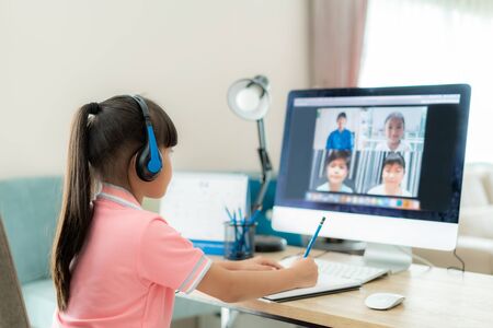 Asian girl student video conference e-learning with teacher and classmates on computer in living room at home. Homeschooling and distance learning ,online ,education and internet.の写真素材
