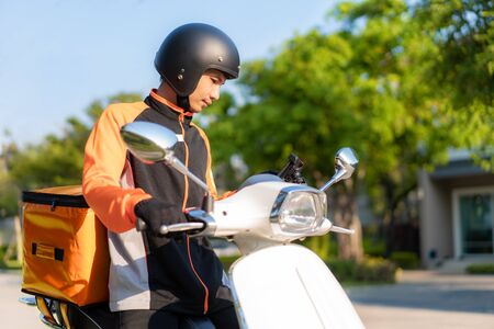 Asian man courier checking customer location in map in smartphone on scooter delivering food in town streets with a hot food delivery from take aways and restaurants to home, express food delivery and shopping online concept.の写真素材