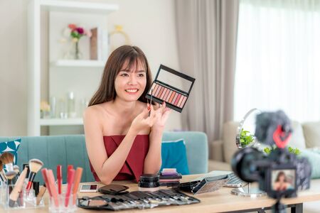 Asian woman vlogger present or teaching make up beauty cosmetic product or her face and broadcast live video to social network by internet at home, beauty blogger concept.の写真素材