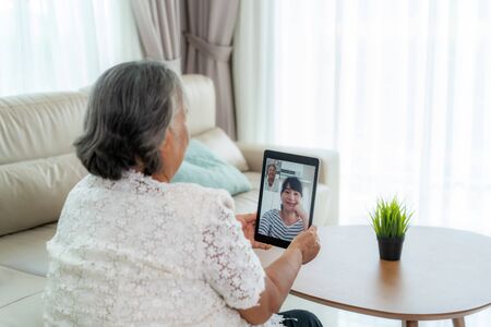 Asian elderly woman virtual happy hour meeting and talking online together with her daughter in video conference with digital tablet for a online meeting in video call for social distancing.の写真素材
