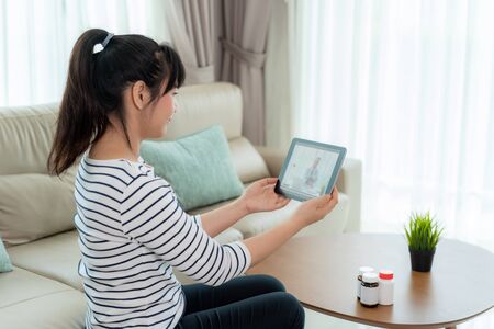 Back view of woman making video call with her doctor while staying at home. Close up of patient in video conferencing with general practitioner on digital tablet. Sick girl in online consultation.の写真素材