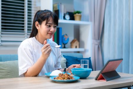 Asian woman virtual happy hour meeting dinner and eating food online together with her boyfriend in video conference with digital tablet for a online meeting in video call for social distancingの写真素材