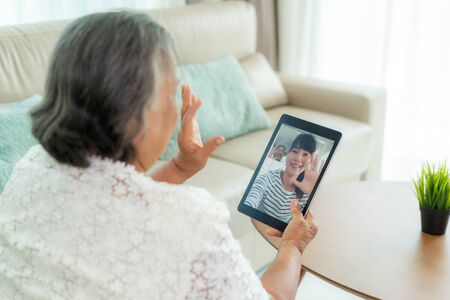 Asian elderly woman virtual happy hour meeting and talking online together with her daughter in video conference with tablet for a online meeting in video call for social distancing.の写真素材