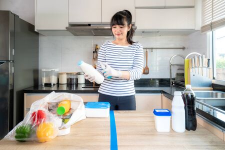 Asian young woman laying out groceries on a divided table and wiping down yogurt or milk containers bottle with disinfectant take to eliminate the chances of contamination COVID-19.の写真素材