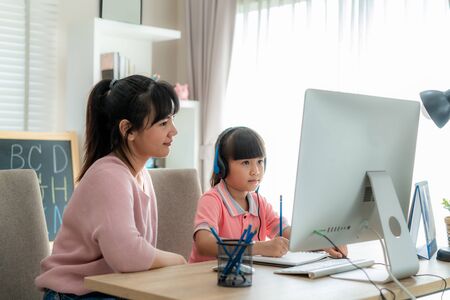 Asian girl student with mother video conference e-learning with teacher on computer in living room at home. Homeschooling and distance learning ,online ,education and internet.の写真素材