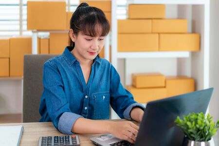 Asian owner business woman work at home for online shopping, chat with customer her notebook with laptop with office equipment, entrepreneur lifestyle conceptの写真素材