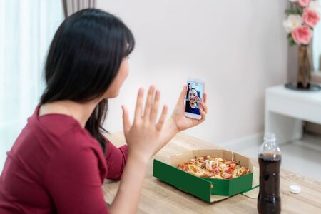 Asian woman virtual happy hour meeting dinner and eating pizza food online together with her boyfriend in video conference with digital tablet for a online meeting in video call for social distancing
の写真素材