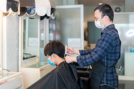 Asian young man and hairdresser man wearing medical mask to protect themselves during novel Coronavirus, Covid-19 in Barbershop Hair Care Service.の写真素材