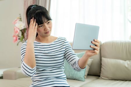 Asian woman making video call with her doctor with her feeling headache on digital tablet online healthcare digital technology service consultation while staying at home.の写真素材