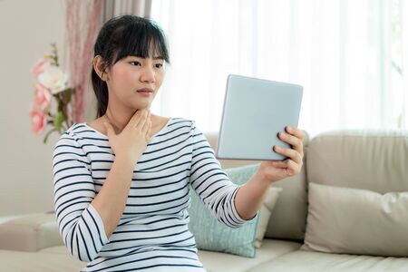 Asian woman making video call with her doctor with her feeling sore throat on digital tablet online healthcare digital technology service consultation while staying at home.の写真素材