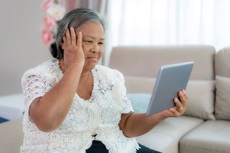 Elderly woman making video call with her doctor with her feeling headache on digital tablet online healthcare digital technology service consultation while staying at home.の写真素材