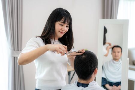 Asian young man with her girlfriend hairdresser cutting hair with Haircutting scissors at home they stay at home during time of home isolation against Novel coronavirus or COVID-19の写真素材