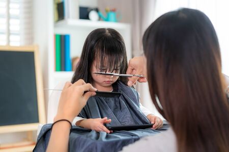 Asian Mother cutting hair to her daughter in living room at home while stay at home safe from Covid-19 Coronavirus during lockdown. Self-quarantine and social distancing concept.の写真素材