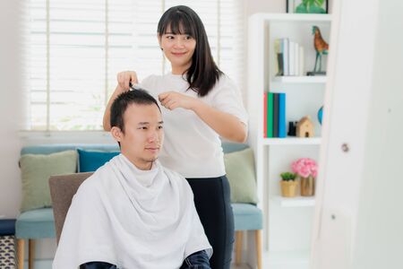 Asian young man with her girlfriend hairdresser cutting hair with an electric hair clipper at home they stay at home during time of home isolation against Novel coronavirus or COVID-19の写真素材