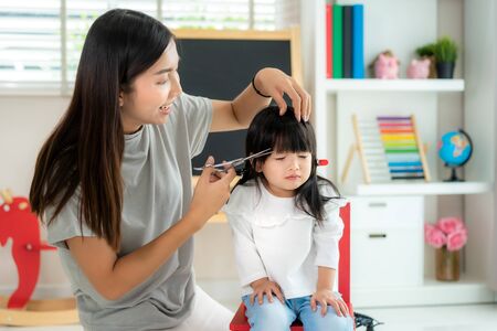 Asian Mother cutting hair to her daughter in living room at home while stay at home safe from Covid-19 Coronavirus during lockdown. Self-quarantine and social distancing concept.の写真素材