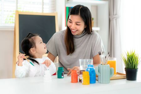 Asian kindergarten schoolgirl with mother painting Plaster doll with Acrylic water color paint in living room at home. Homeschooling and distance learning.の写真素材