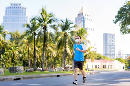 Asian young man are jogging and exciseing outdoor in city park and wearing protective mask on face for stay in fit during Covid-19 pandemic in Bangkok, Thailand.の写真素材
