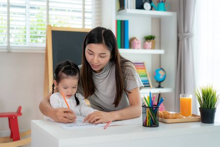 Asian kindergarten student girl with mother painting picture in book with color pencil at home, Homeschooling and distance learning.
の写真素材