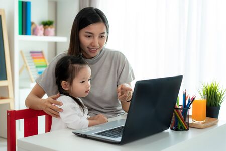 Asian kindergarten school girl  with mother video conference e-learning with teacher on laptop in living room at home. Homeschooling and distance learning ,online ,education and internet.の写真素材